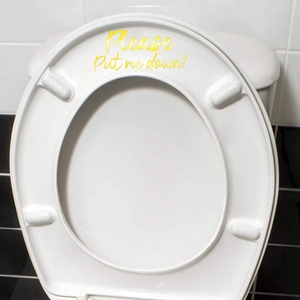 Golden 'Please Put me down!' wall sticker applied on a white toilet lid in bathroom