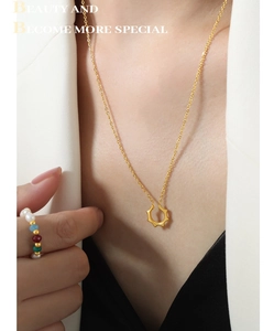 Détail d'un collier doré à pendentif géométrique en U avec une bague en perles colorées