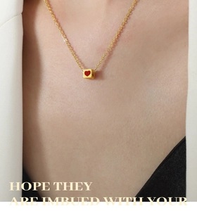 Detail of red heart cube pendant on a golden chain necklace worn by a model