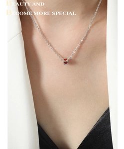 Macro detail of silver necklace featuring a cube pendant with red heart patterns