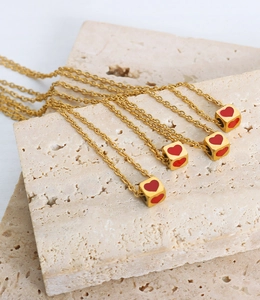 Detail of four gold necklaces with red heart dice pendants on a beige stone surface