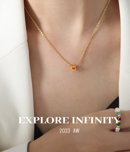 Detail of gold necklace with red heart pendant and colorful pearl bead ring on model