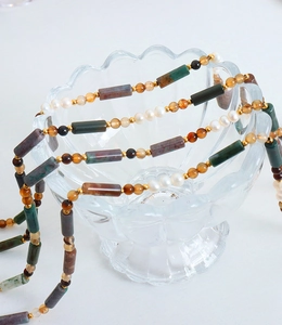 Détail d'un collier en pierre naturelle et perles d'eau douce sur un bol en verre