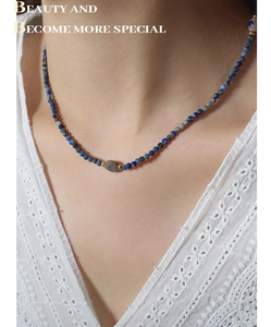 Detail of beaded necklace with blue natural stones and irregular grey gemstone on lace top