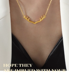 Vue détaillée d'un collier doré avec pendentif en bois de cerf porté sur une tenue chic