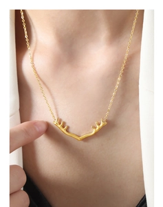 Gros plan d'un collier pendentif bois de renne doré porté sur une chaîne fine