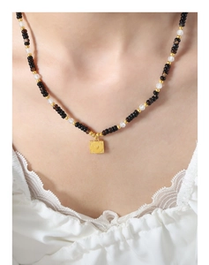 Detailed view of beaded necklace with black stones and heart embossed gold pendant