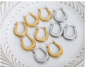 Close-up of textured gold and silver U-shaped earrings on a white porcelain plate