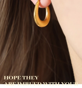 Close-up of golden U-shaped earrings with spiral texture shown on model ear