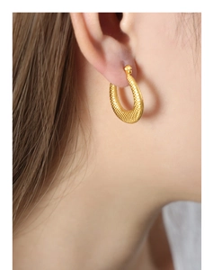 Detailed view of gold U-shaped earrings with textured granular finish on earlobe