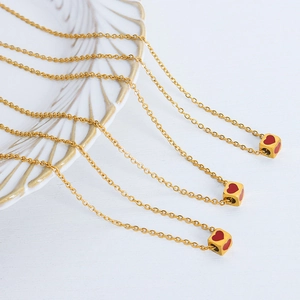 Three gold stainless steel necklaces featuring dainty red heart cube pendants on white background