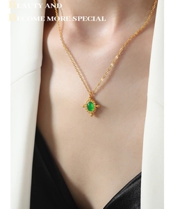 Détail d'un collier vintage doré avec pendentif gemme ovale verte porté sur mannequin