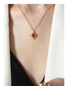Détail d'un collier vintage doré avec pendentif en pierre rouge porté sur un mannequin