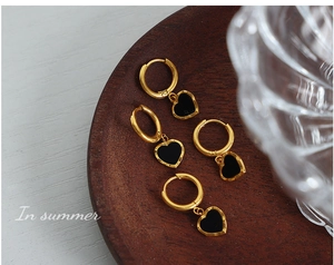 Détail de boucles d'oreilles en acier titane doré avec cœurs en acrylique noir sur bois
