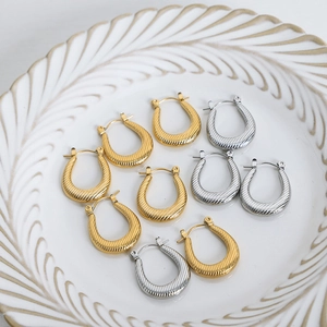 U-shaped striped earrings in gold and silver finish displayed on a white ceramic plate
