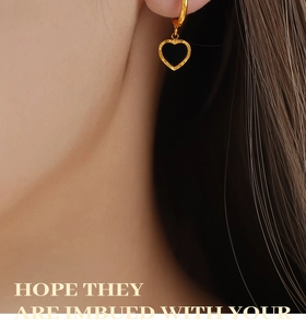 Détail de boucles d'oreilles cœur dorées avec incrustation noire et effet martelé