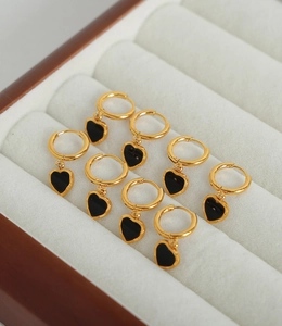 Détail de créoles dorées avec pendentifs en forme de cœur noir dans un écrin à bijoux