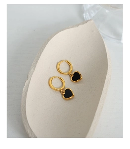 Détail de boucles d'oreilles créoles dorées avec cœurs noirs sur un plateau en céramique