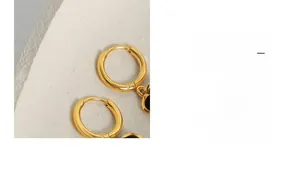 Détail de boucles d'oreilles créoles dorées 18k avec trèfle noir dans un bol en céramique