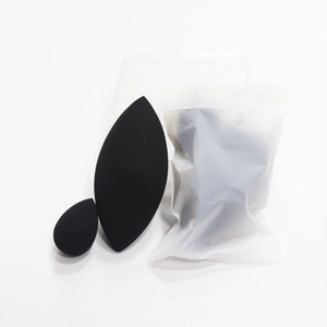 Detail of two black makeup sponges including olive-cut shape and frosted packaging bag