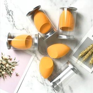 Detailed view of 5 orange makeup sponges in a clear cylinder storage case with silver lid
