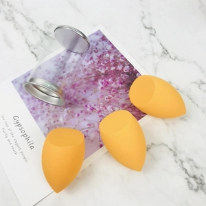Three orange beauty blenders in a clear storage tube on marble background