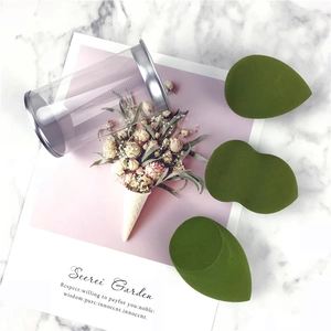 Three green makeup sponges in teardrop and cut shapes with a clear storage canister
