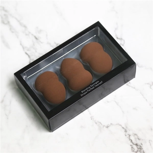 Trois éponges de maquillage marron dans une boîte noire à fenêtre sur marbre