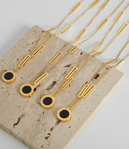 Detail of gold titanium steel necklaces with Roman numeral charms on beige stone