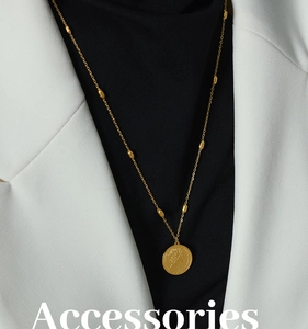 Close-up of gold coin pendant necklace featuring Queen Elizabeth portrait on white blazer