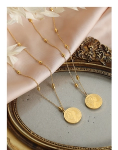 Close-up of 18k gold coin necklace with embossed portrait and elegant beaded chain
