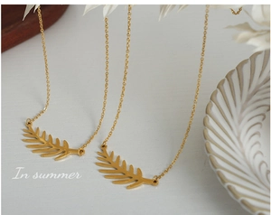 Detalle de colgantes de hoja en acero de titanio chapado en oro 18k sobre fondo blanco