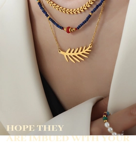 Detalle del collar con colgante de hoja dorada y collares de cuentas azules y rojas