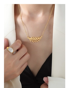 Primer plano de collar con colgante de hoja dorada y anillo de nácar en modelo