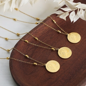 Elegant vintage gold plated titanium steel coin necklaces with beads on a wood tray