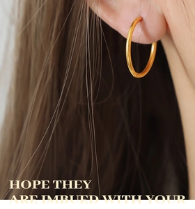 Close-up of minimalist gold-plated titanium hoop earrings on a model with a matte finish