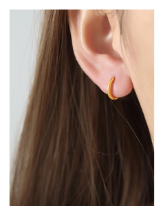 Close-up of minimalist 18k gold hoop earrings worn on a model with long brown hair