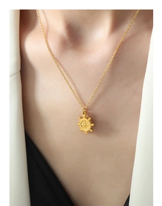 Gros plan d'un collier pendentif gouvernail doré porté par un mannequin en costume