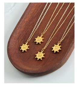 Détail de quatre colliers avec pendentif gouvernail doré sur plateau en bois foncé