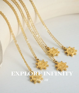 Gros plan de colliers dorés avec pendentif gouvernail et gravure Explore Infinity