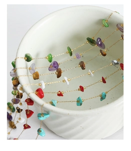 Detail of layered gold necklace with colorful natural gemstones on white ceramic