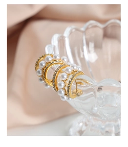 Détail de boucles d'oreilles C dorées avec perles blanches et strass scintillants