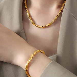 Golden baroque chain necklace and bracelet set shown on model in khaki suit