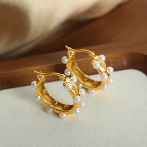 Boucles d'oreilles créoles dorées géométriques avec perles blanches sur plateau en bois