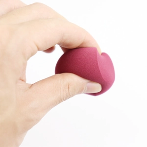 Close-up of wine red makeup sponge being squeezed to show soft and bouncy texture