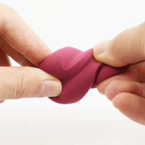 Detailed close-up of dark red beauty sponge being twisted to show soft elasticity