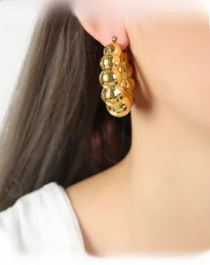 Détail macro de boucles d'oreilles dorées en U avec design à sphères et fini miroir