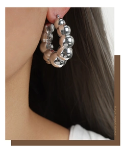 Gros plan d'une boucle d'oreille créole à billes d'argent poli portée par une femme