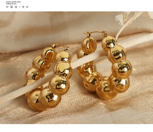 Gros plan de boucles d'oreilles créoles dorées à billes sur fond de soie champagne