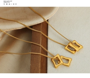 Détail de deux pendentifs carrés dorés entrelacés sur soie et bois, collier élégant